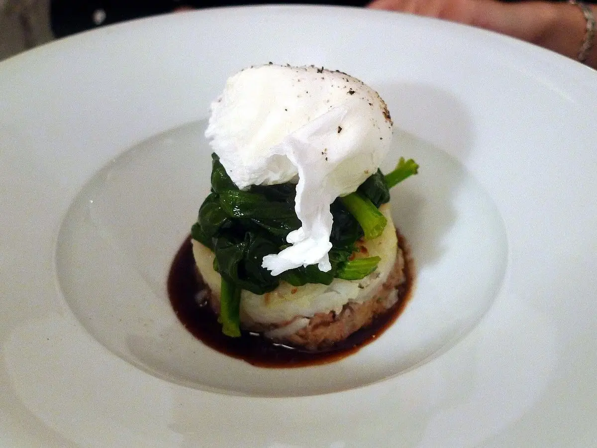 Torre de hash de patata con espinacas y un huevo poché encima sobre un plato hondo blanco