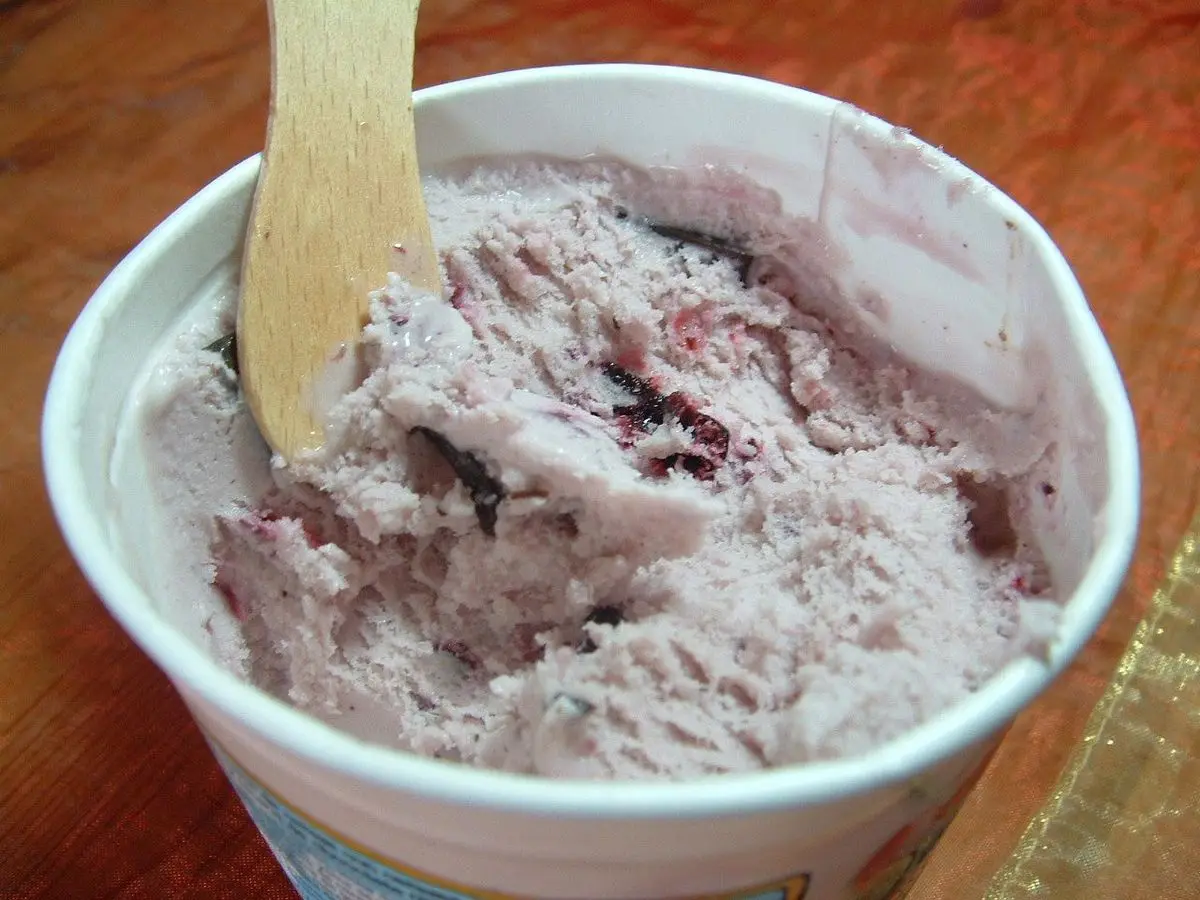 Vasito blanco con helado de cereza con trocitos de fruta y chocolate y una cuchara de madera