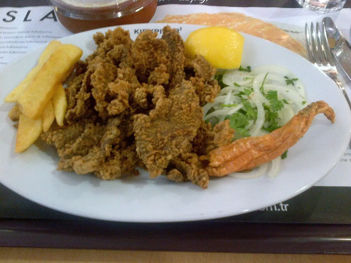 Plato con hígado frito en trozos, ensalada de cebolla con perejil, limón y patatas fritas