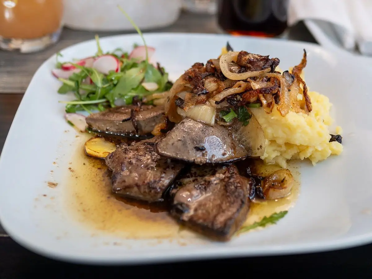 Plato con hígado salteado con cebolla sobre puré de patata y ensalada con rábanos