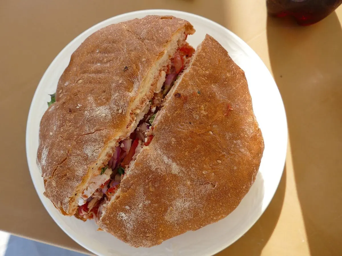 Pan maltés redondo abierto por la mitad relleno de atún, tomate y verduras sobre un plato blanco