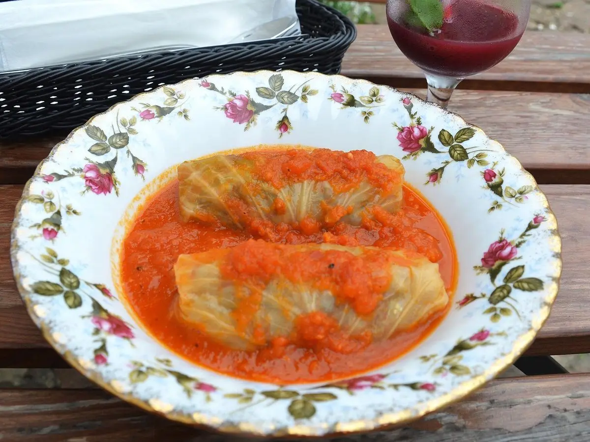 Rollo de hoja de col relleno en salsa de tomate sobre un plato blanco con flores