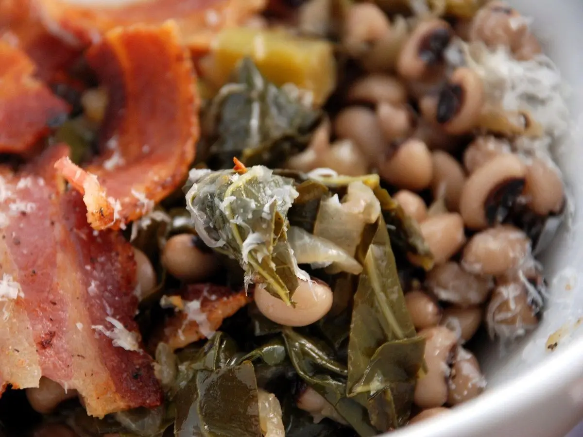 Judías carillas guisadas con panceta, verduras de hoja y queso rallado en un cuenco