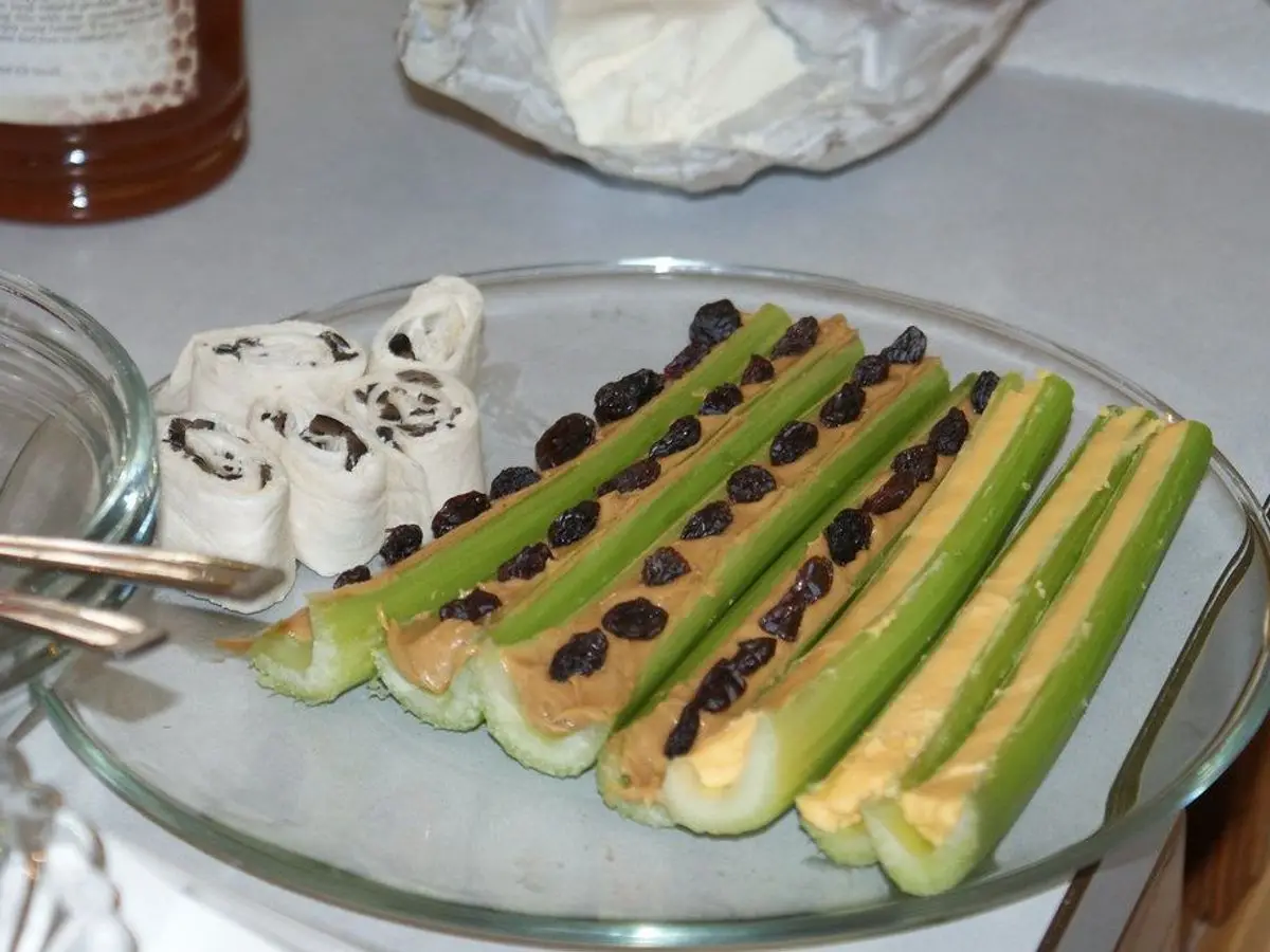 Tallos de apio rellenos de crema de frutos secos y cubiertos de pasas, sobre una fuente de cristal
