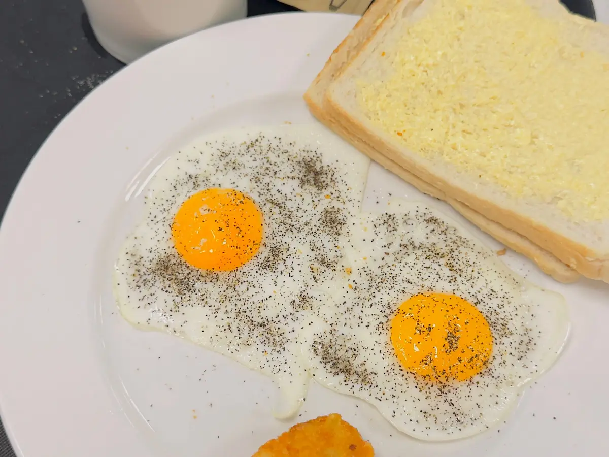 Dos huevos fritos con tostada y croqueta de patata en un plato blanco