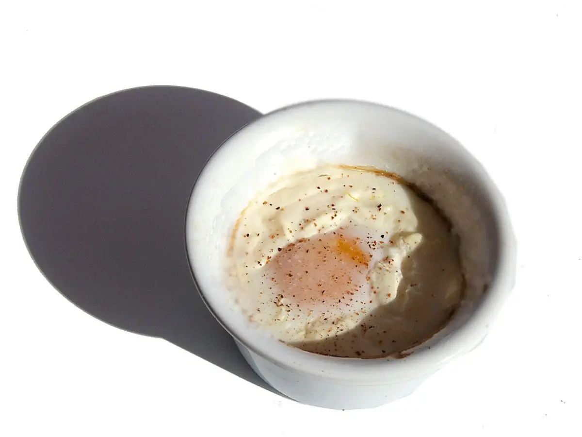 Huevo cocinado en un ramequín blanco individual sobre fondo blanco