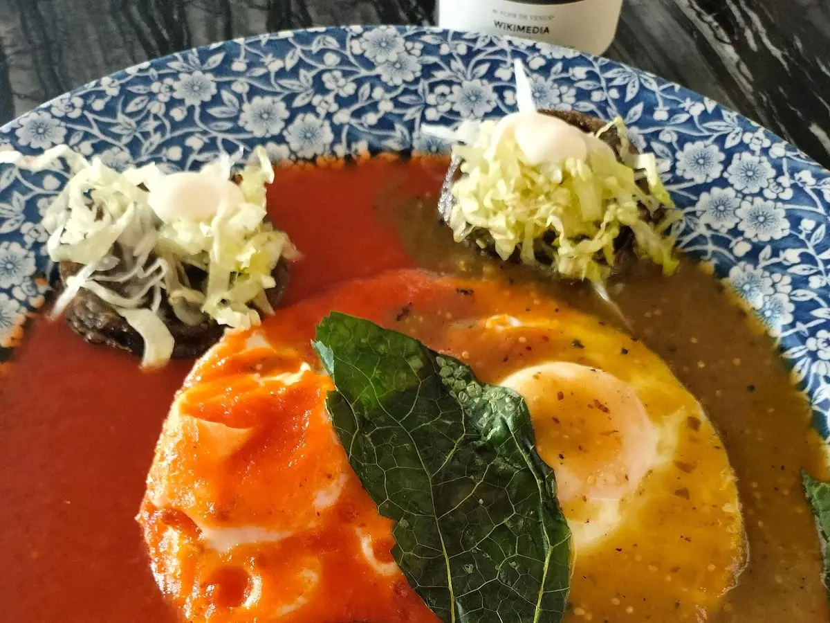 Huevos estrellados sobre tortilla con salsa roja y salsa verde, una hoja verde y col picada