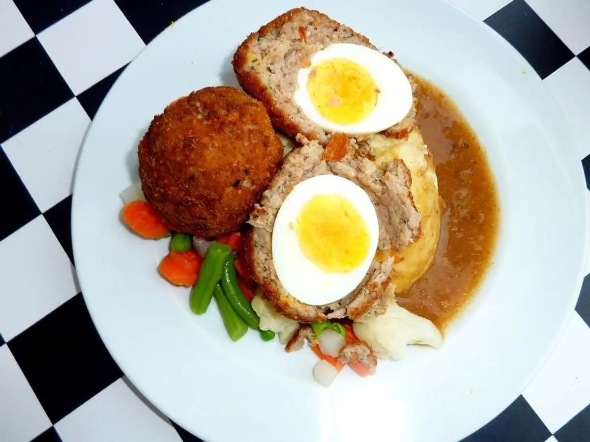 Huevos escoceses abiertos por la mitad con yema cremosa, con verduras y salsa en un plato blanco