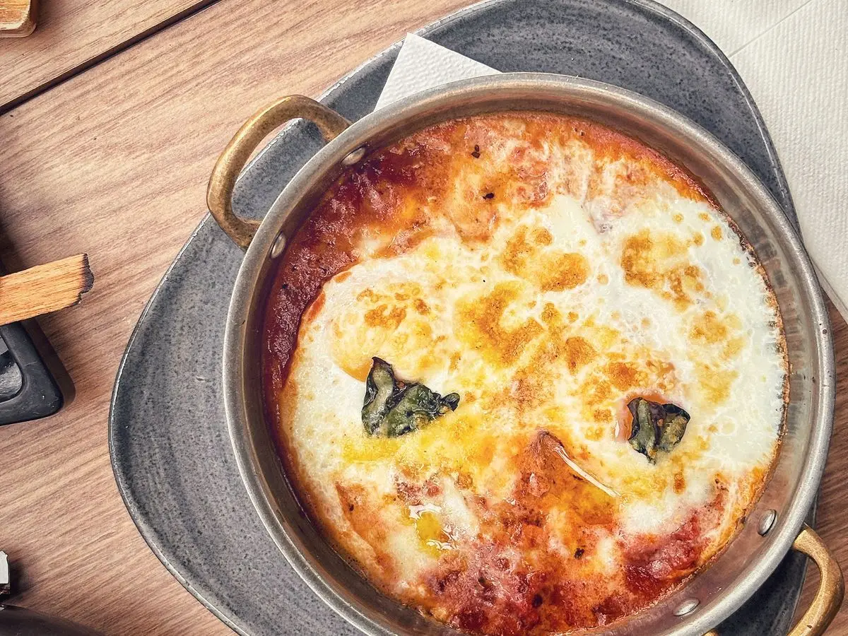 Huevos cuajados al horno sobre salsa de tomate con hojas de albahaca en una cazuela metálica