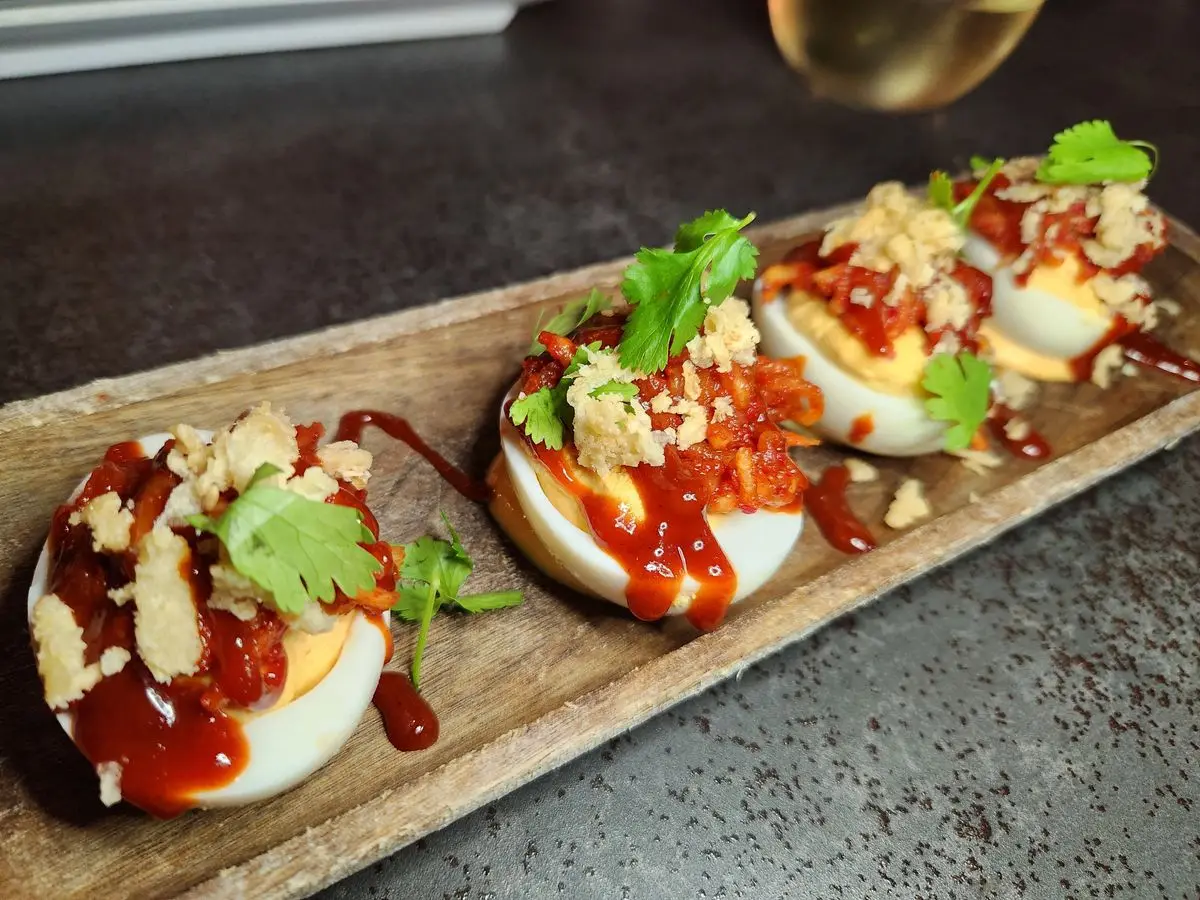 Huevos rellenos con salsa roja, cilantro y queso rallado sobre una tabla de madera alargada