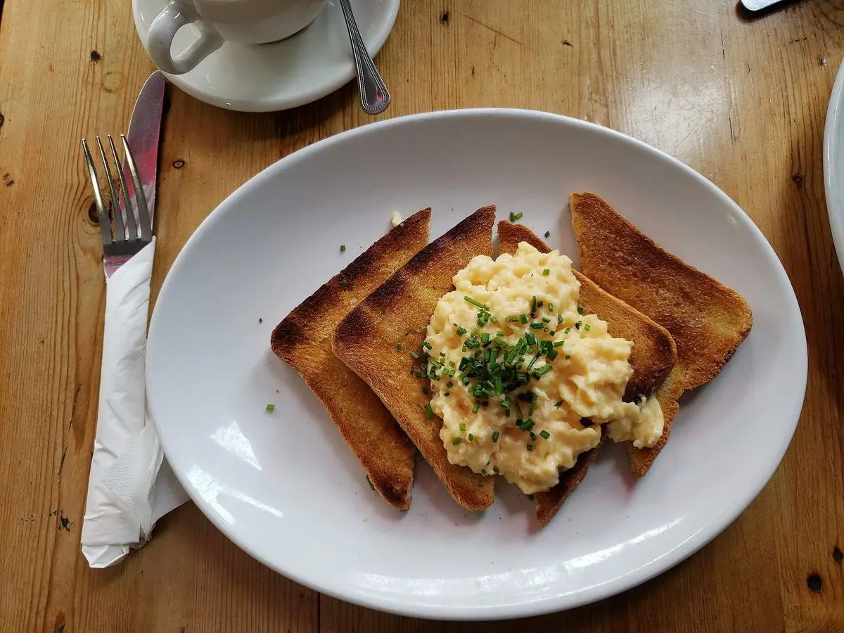 Huevos revueltos con cebollino sobre tostadas en un plato ovalado junto a una taza de café