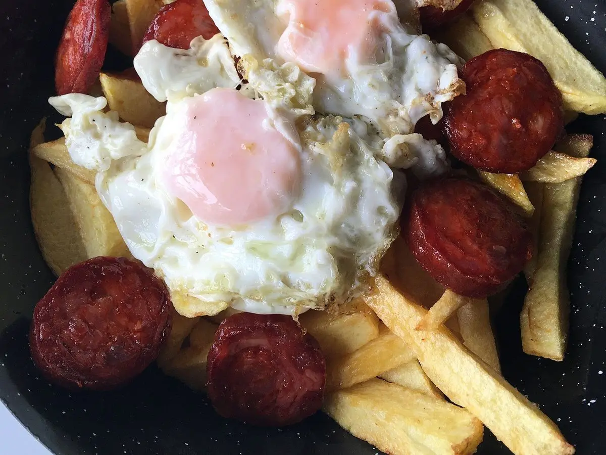 Huevos fritos con rodajas de chorizo y patatas fritas en una sartén negra