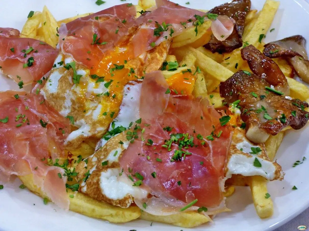 Patatas fritas con huevos rotos y lonchas de jamón y hierbas por encima