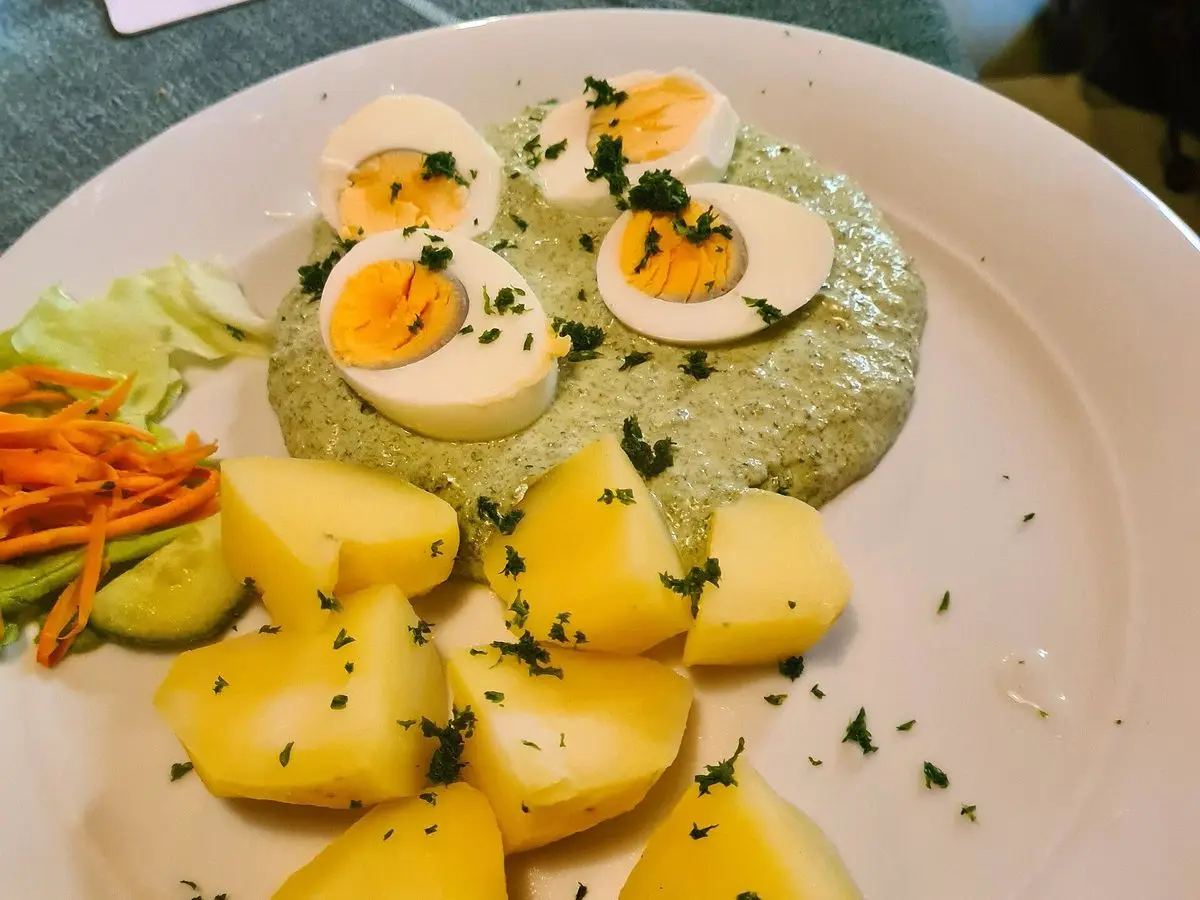 Plato con huevos duros partidos, patatas cocidas y salsa verde de hierbas