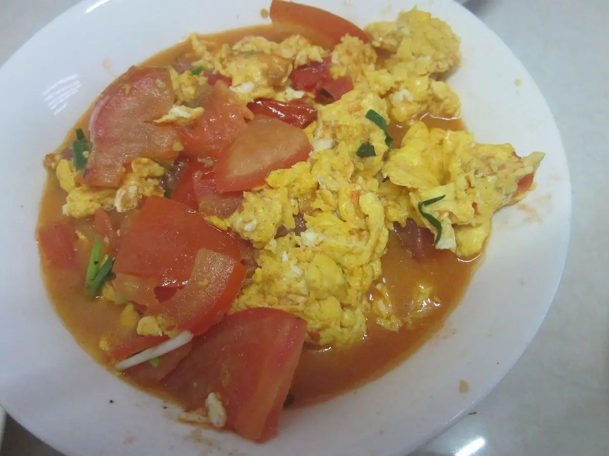 Plato blanco de huevos revueltos con trozos de tomate en salsa roja