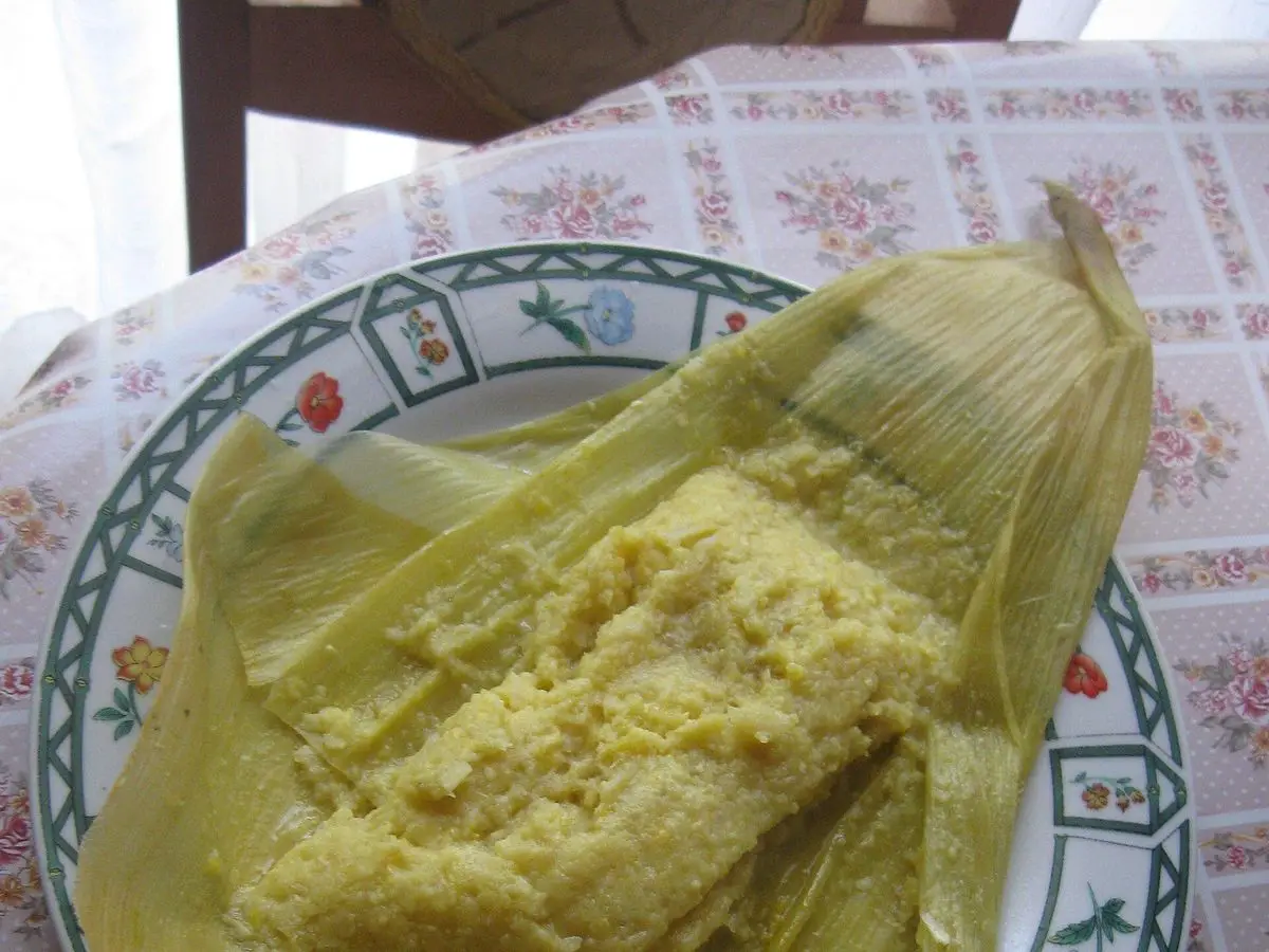 Humita de maíz tierno abierta sobre su hoja de maíz, en un plato con borde decorado