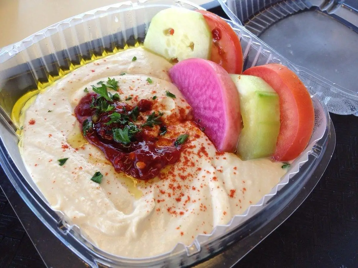 Hummus cremoso con pimentón y hierbas acompañado de rodajas de pepino, tomate y rábano