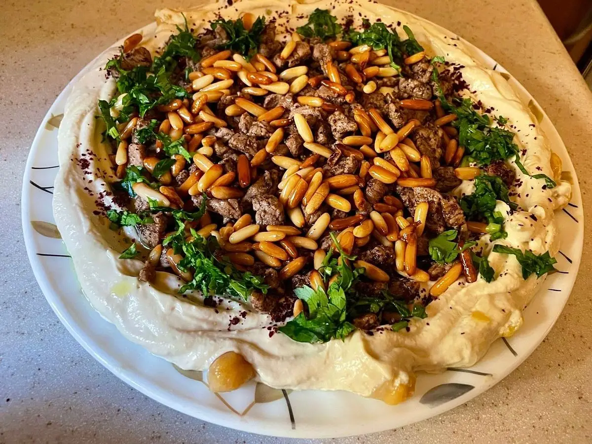 Hummus cubierto de carne especiada, piñones tostados y perejil en un plato blanco