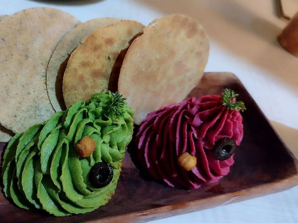 Cremas verde y morada en forma de rosetón sobre una tabla de madera con crackers redondos