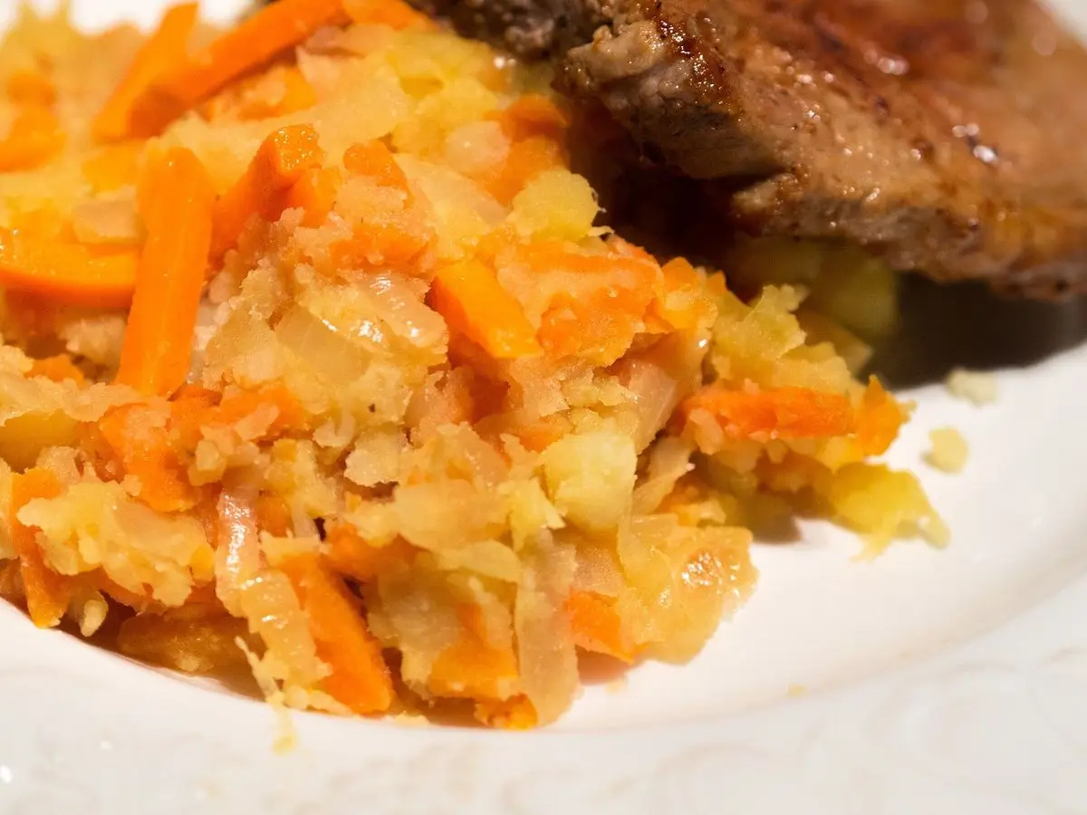 Puré de patata, zanahoria y cebolla con una pieza de carne guisada en un plato blanco