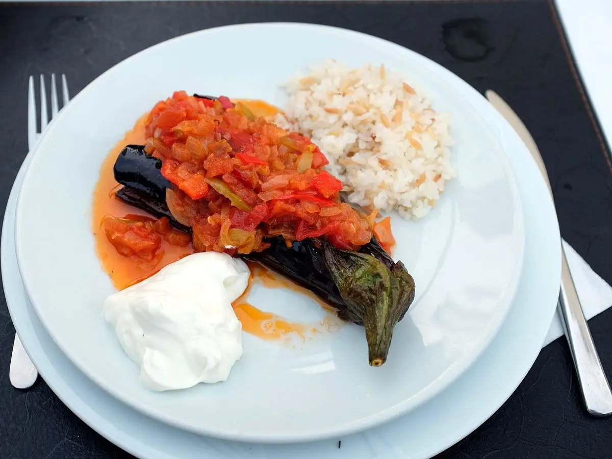Berenjena rellena de tomate y cebolla con una cucharada de yogur y arroz en un plato blanco