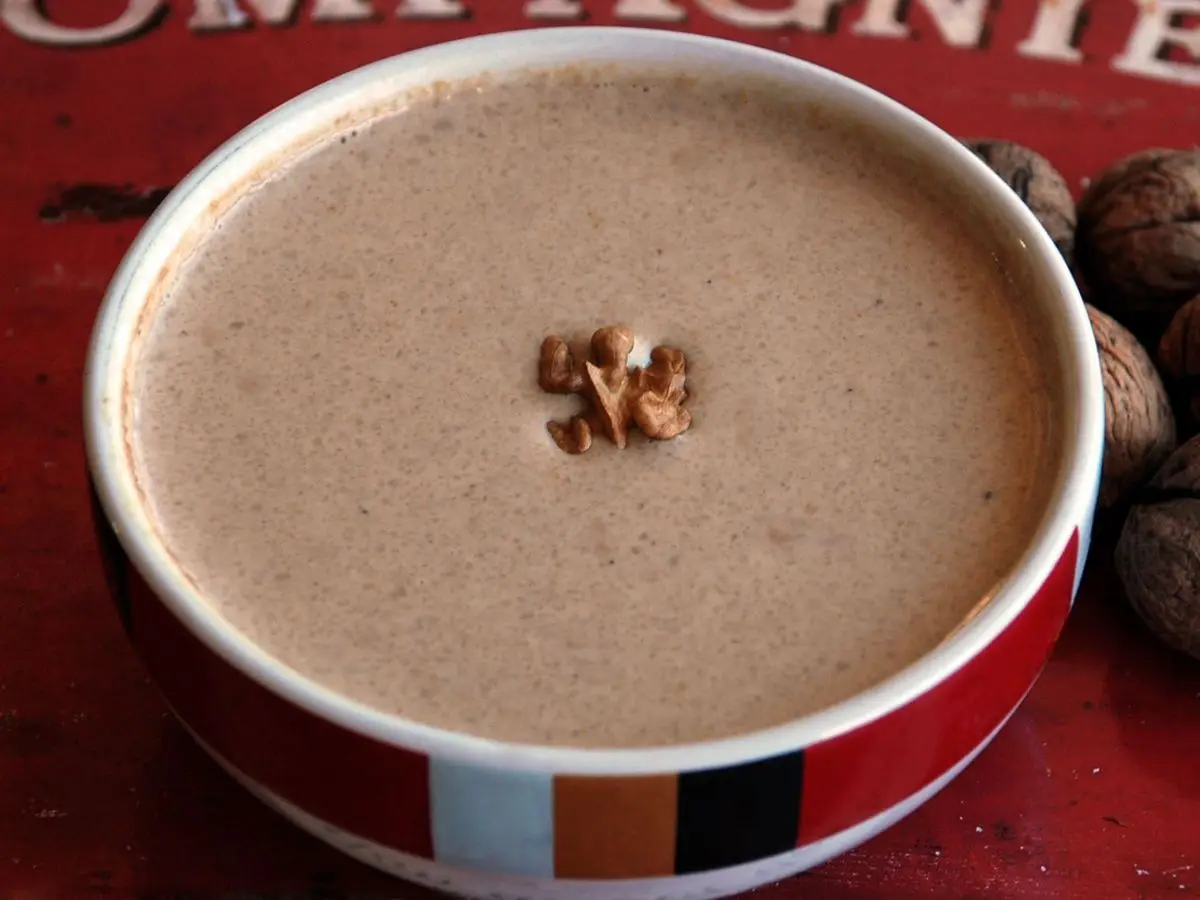 Cuenco con crema beige de nueces con media nuez en el centro y nueces enteras al lado
