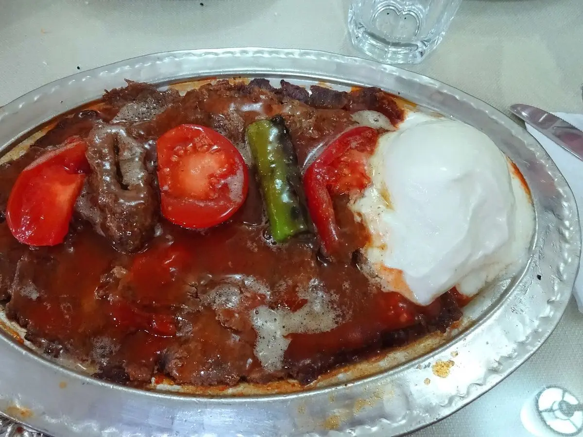 Carne en tiras con salsa de tomate, tomates asados, pimiento verde y yogur sobre una fuente metálica