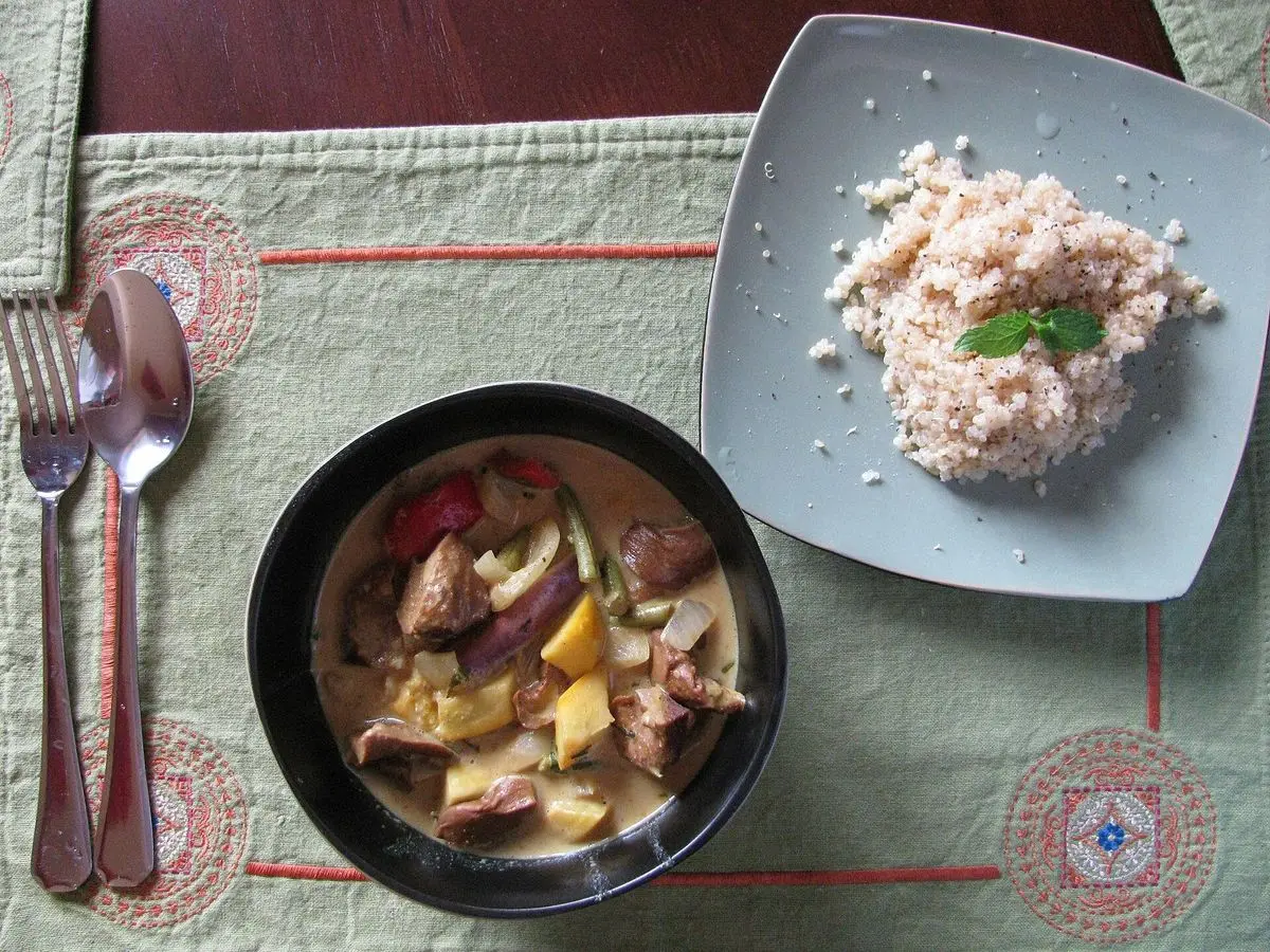 Cuenco negro de guiso vegetal con coco junto a un plato de arroz
