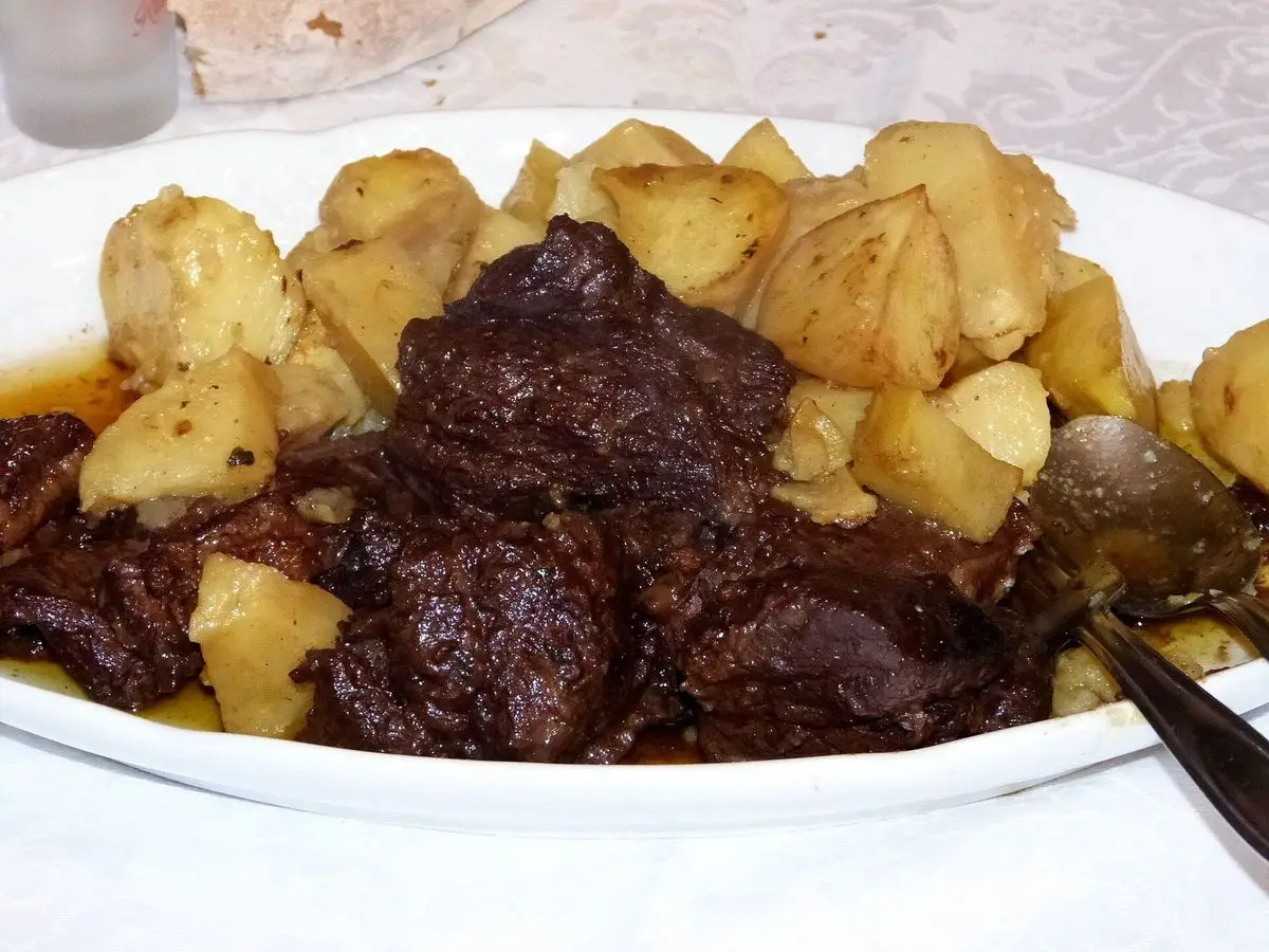 Fuente blanca con estofado de jabalí en salsa oscura y patatas cocidas