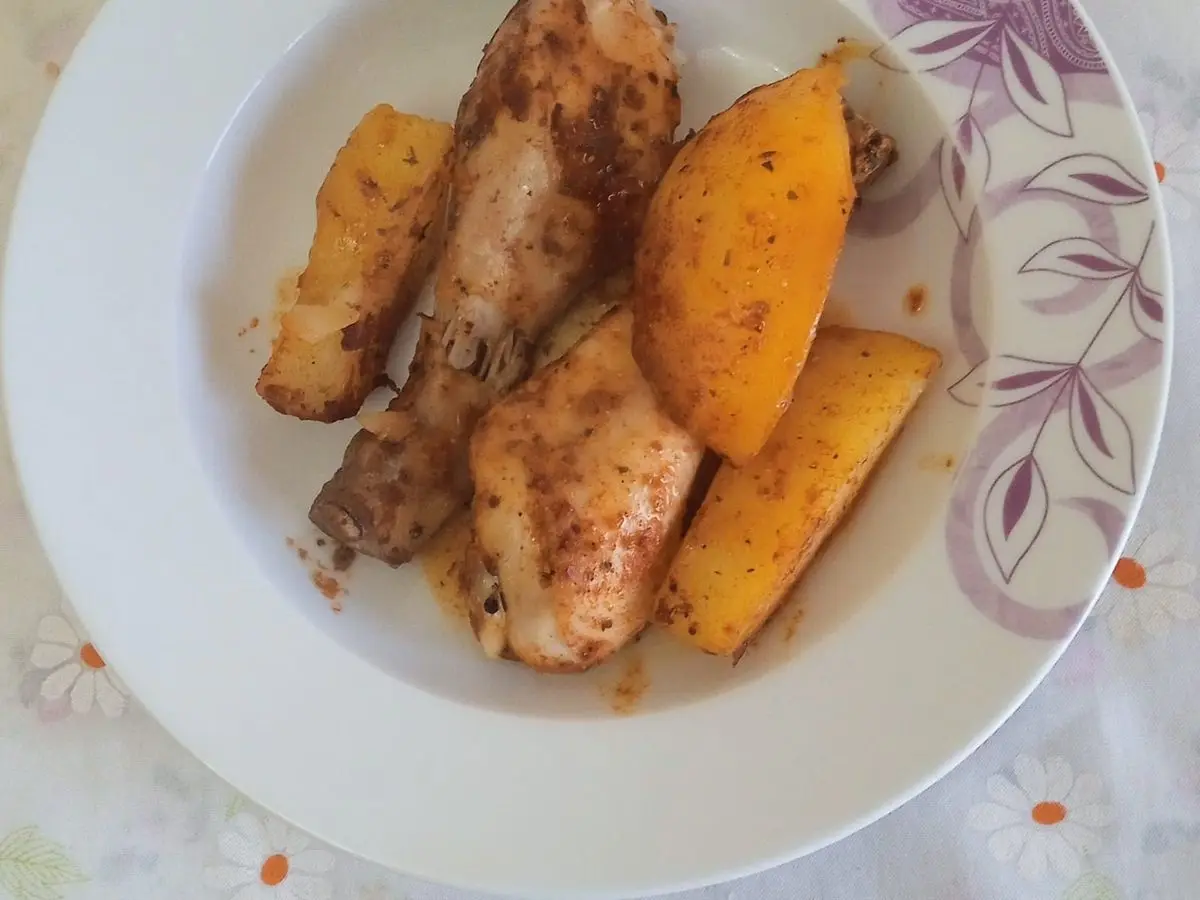 Muslos de pollo asados con patatas doradas en un plato blanco decorado