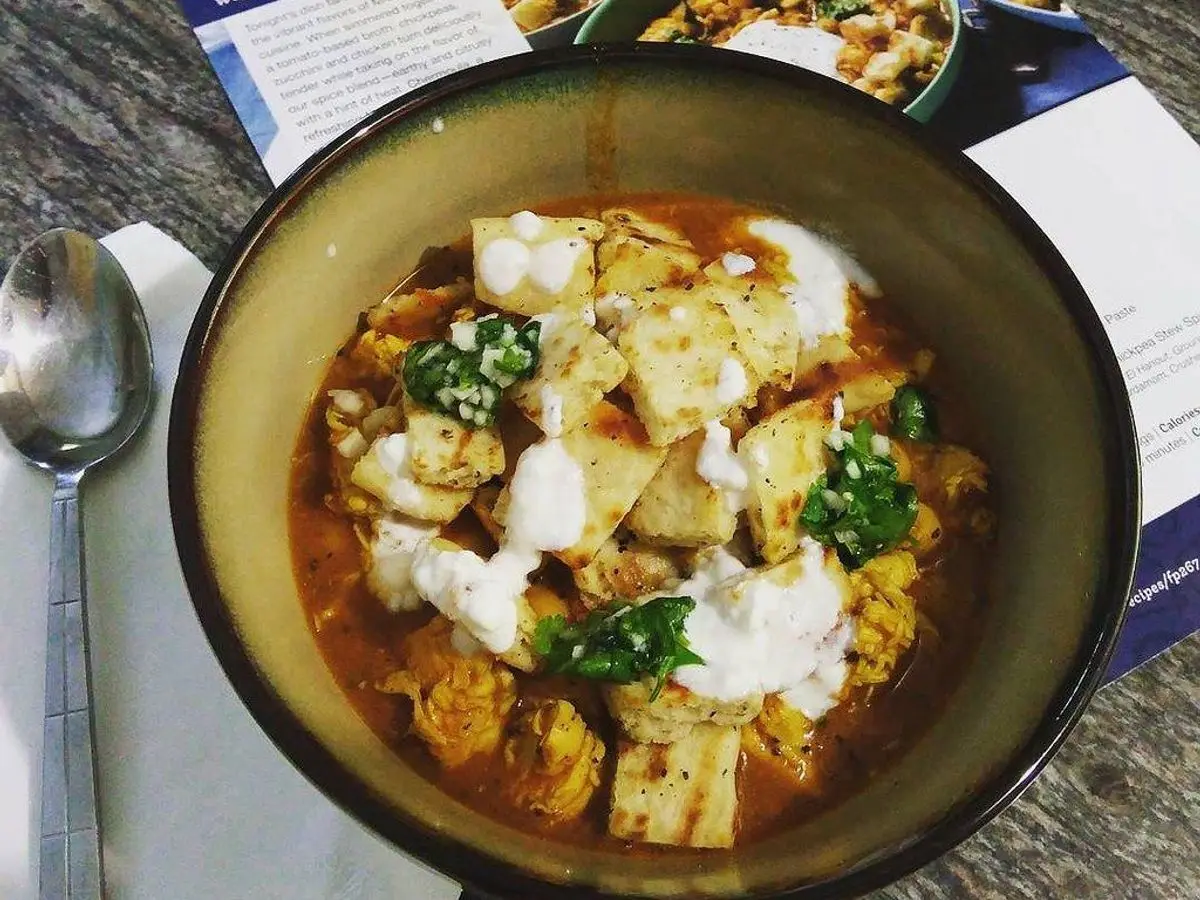 Cuenco con guiso de pollo y garbanzos en salsa de tomate con hierbas, junto a una cuchara