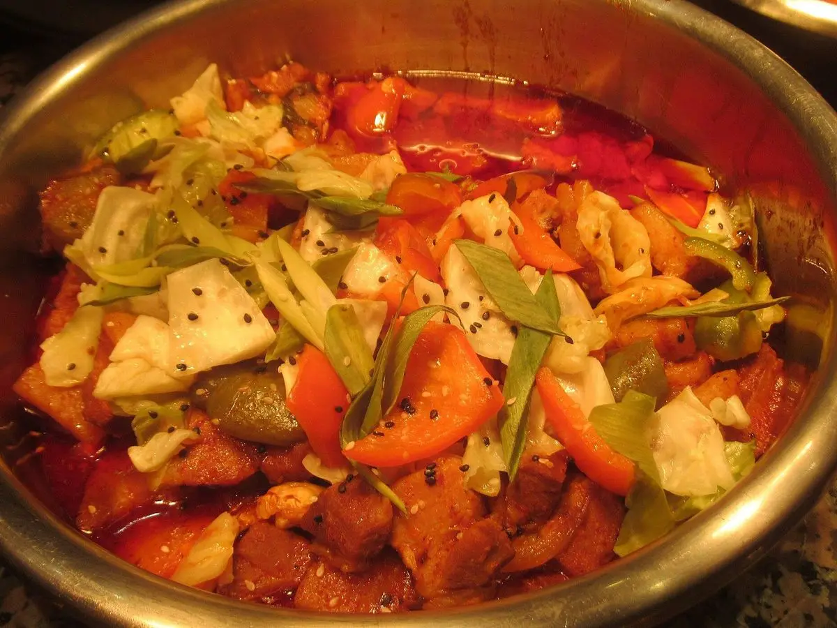 Sartén con cerdo picante salteado con col, pimiento rojo y verduras en salsa roja