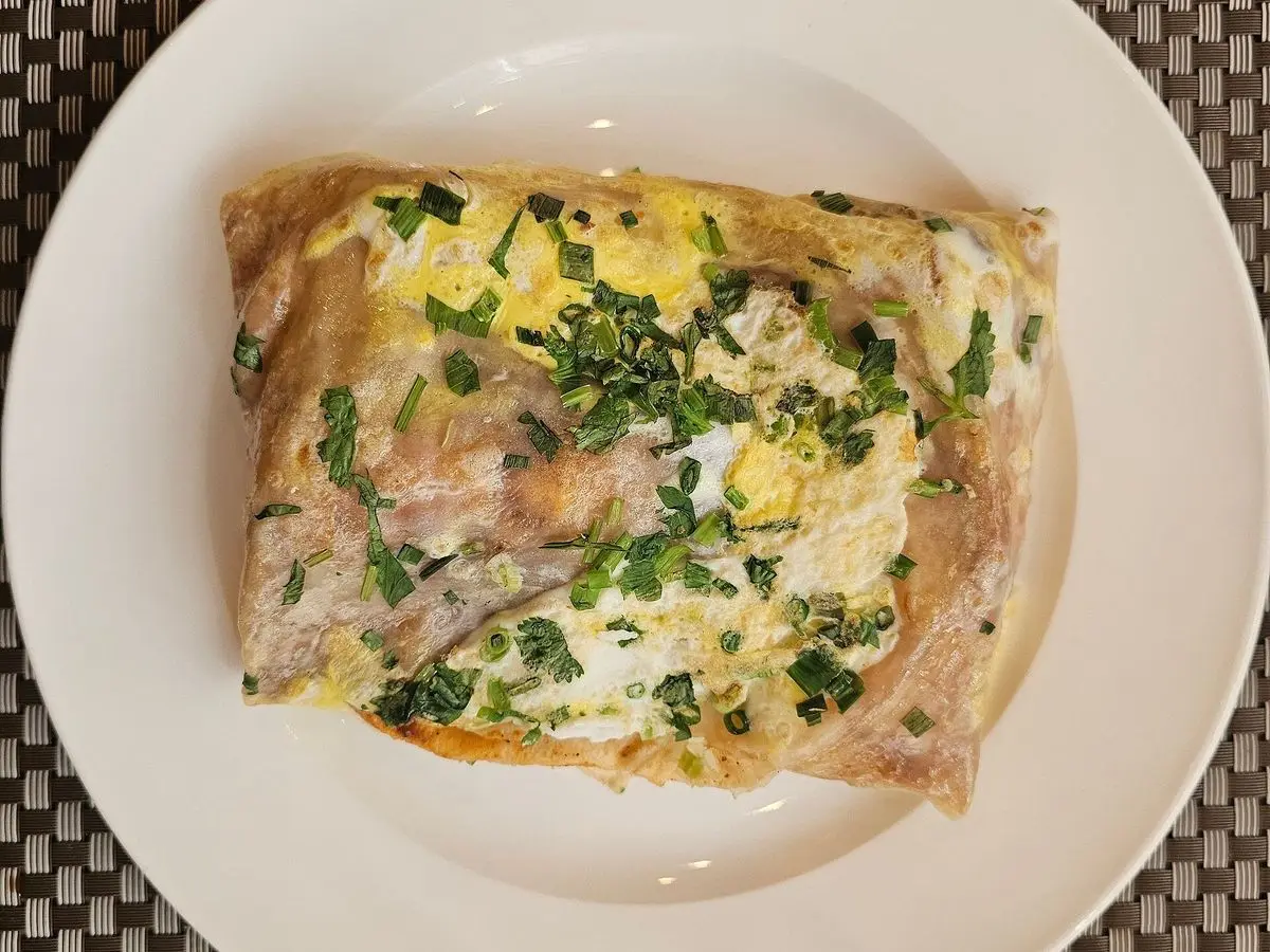 Crepe chino doblado con huevo y cebolleta picada sobre un plato blanco
