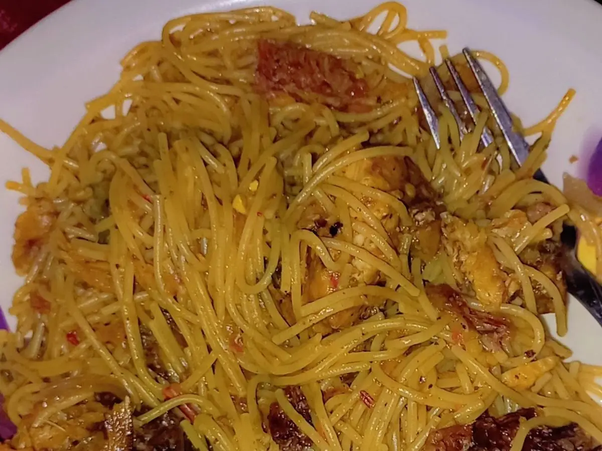 Espaguetis jollof de color naranja con trozos de pollo asado oscuro en un plato