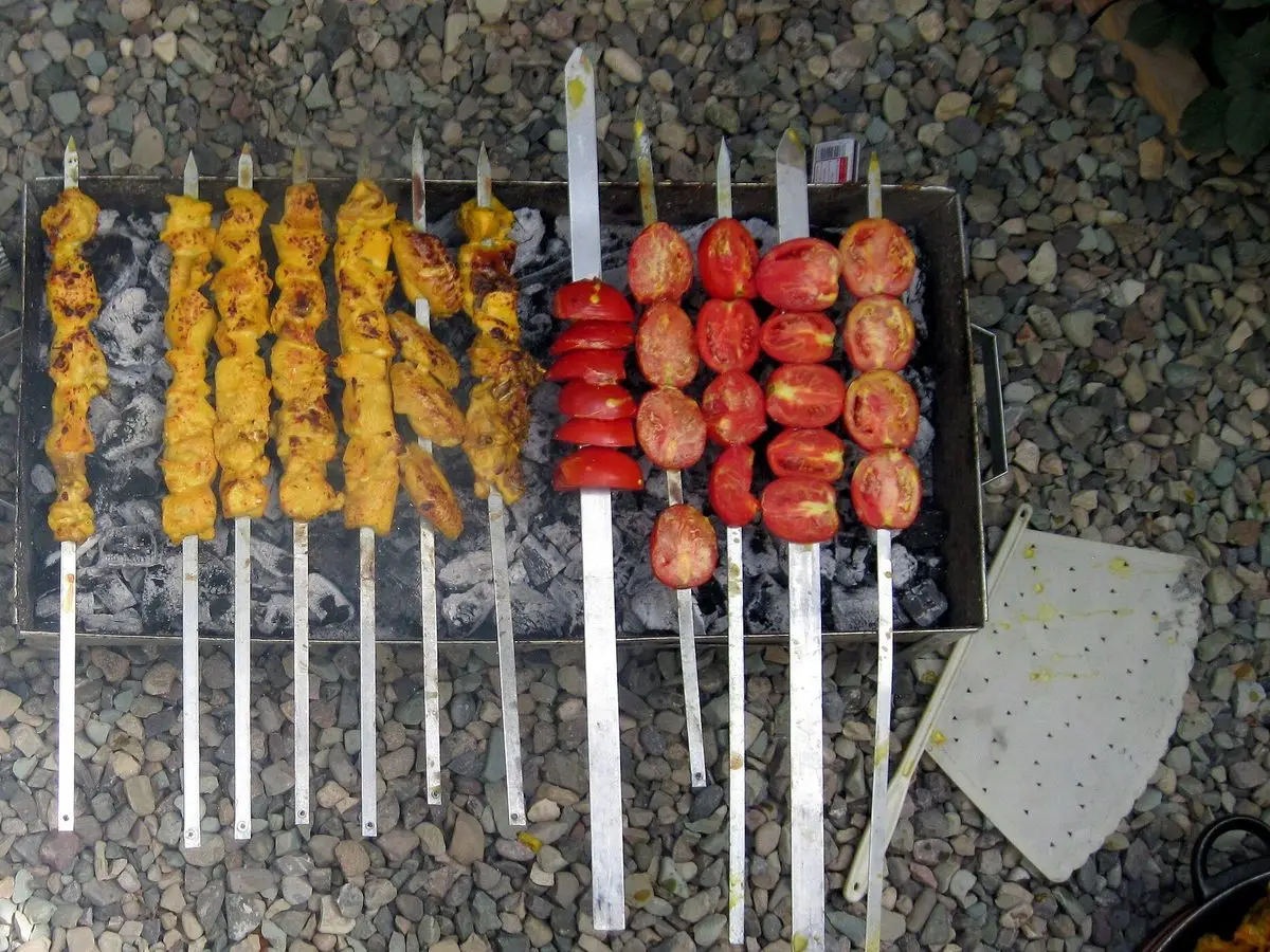 Brochetas de pollo amarillas al azafrán y brochetas de tomates rojos asándose sobre brasas