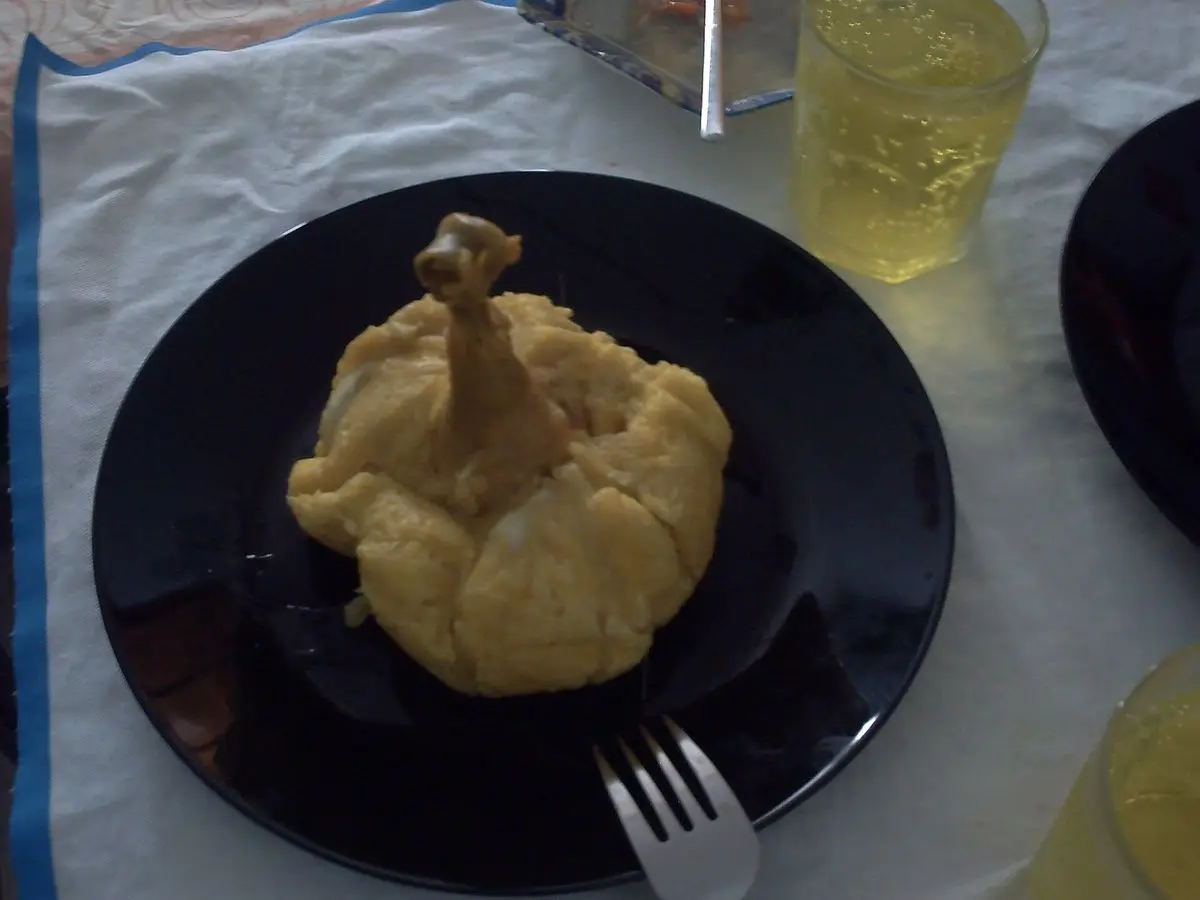 Juane de arroz amarillo con muslo de pollo asomando, servido en un plato negro