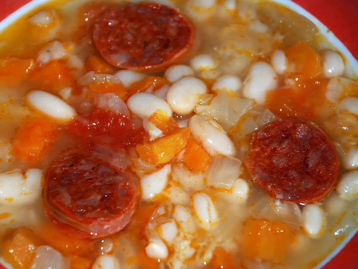Guiso de alubias blancas con rodajas de chorizo y trozos de zanahoria en caldo rojizo