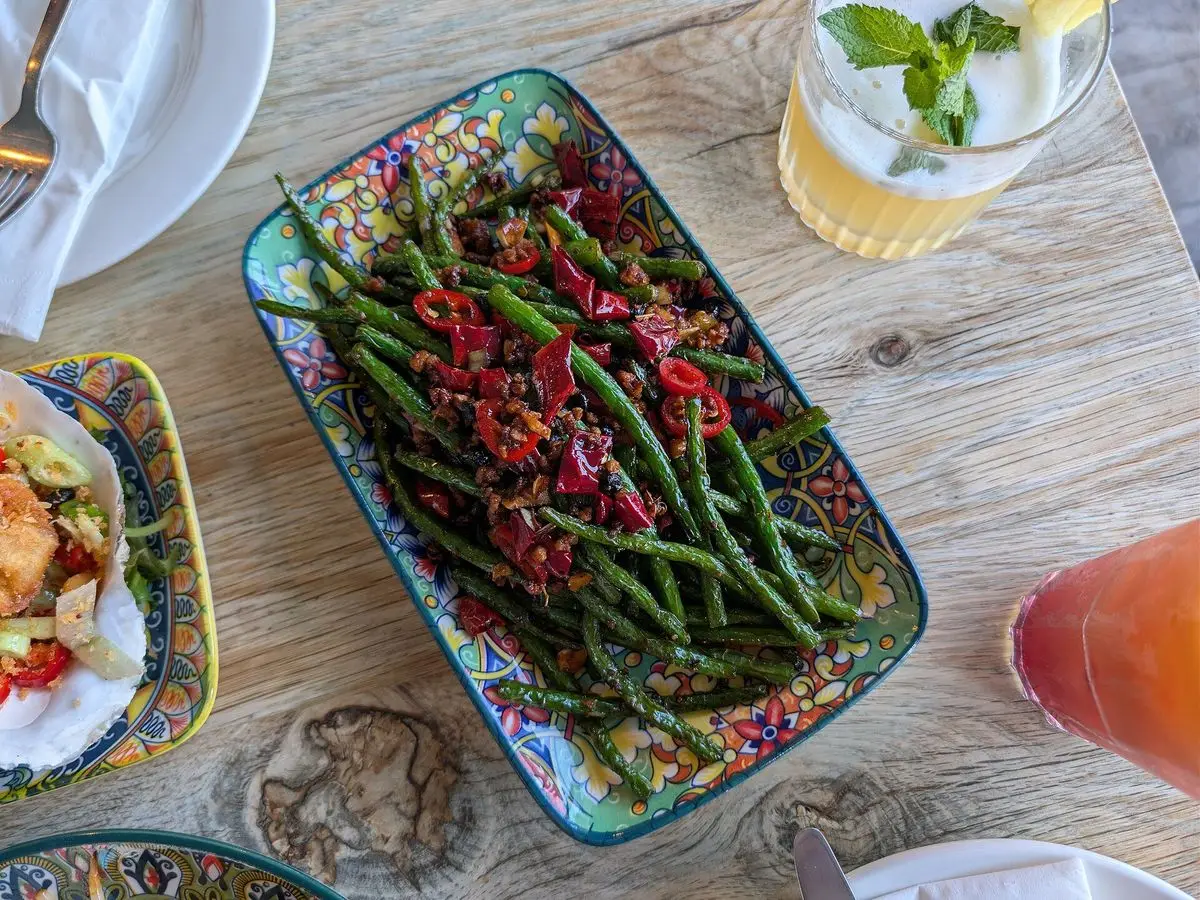Fuente decorada con judías verdes salteadas con guindillas rojas sobre mesa de madera