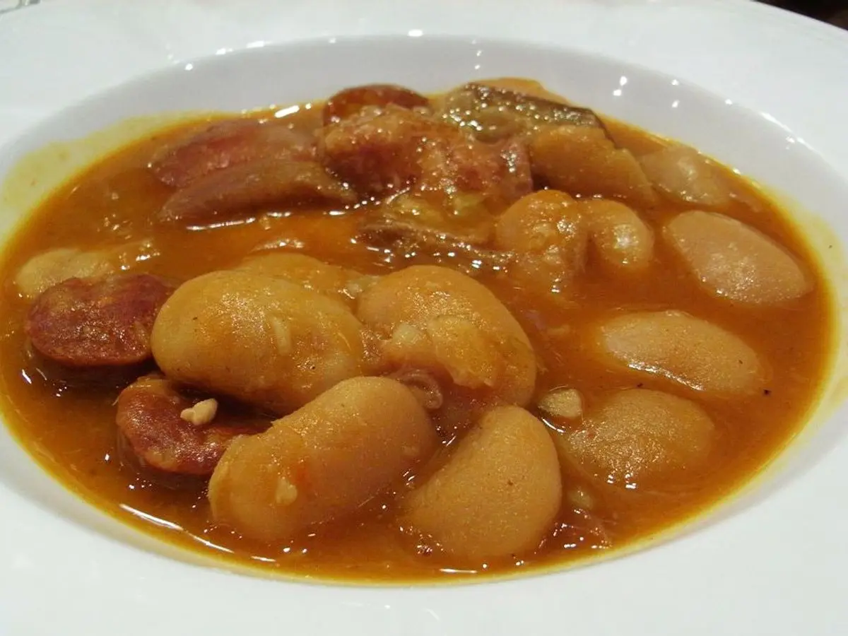 Plato hondo de judiones con trozos de carne y chorizo en caldo anaranjado