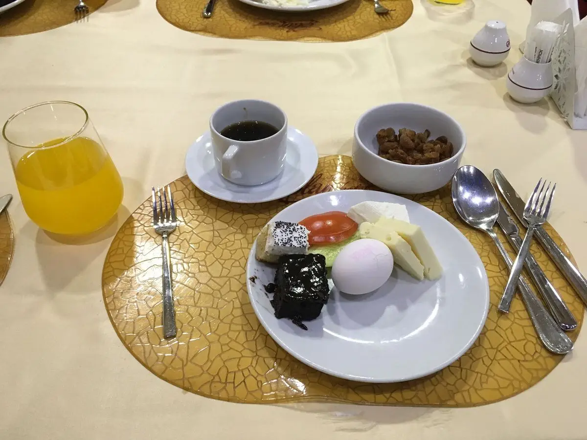 Plato de desayuno turco con huevo cocido, queso blanco, tomate, pepino y aceitunas, junto a un café y zumo