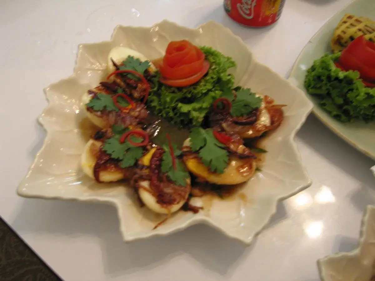 Plato blanco de huevos fritos en salsa de tamarindo con cebolla frita y hierbas