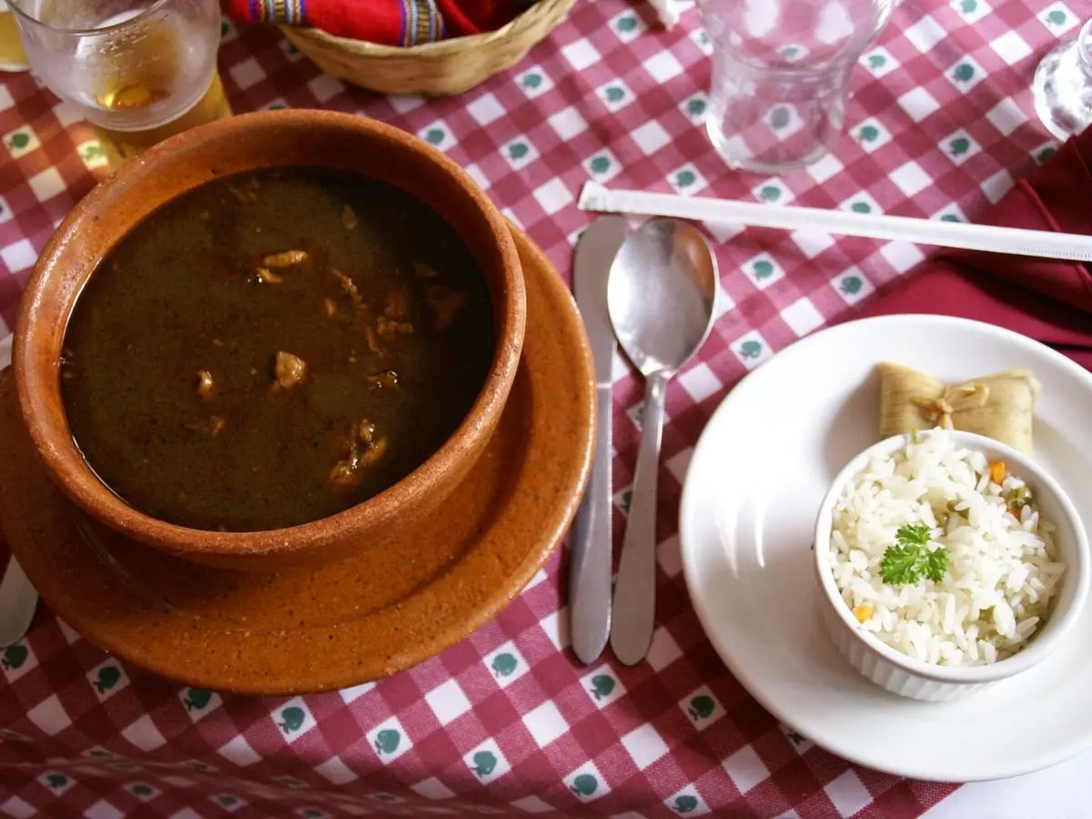 Cuenco de barro con caldo oscuro de pavo kak'ik junto a un plato de arroz blanco