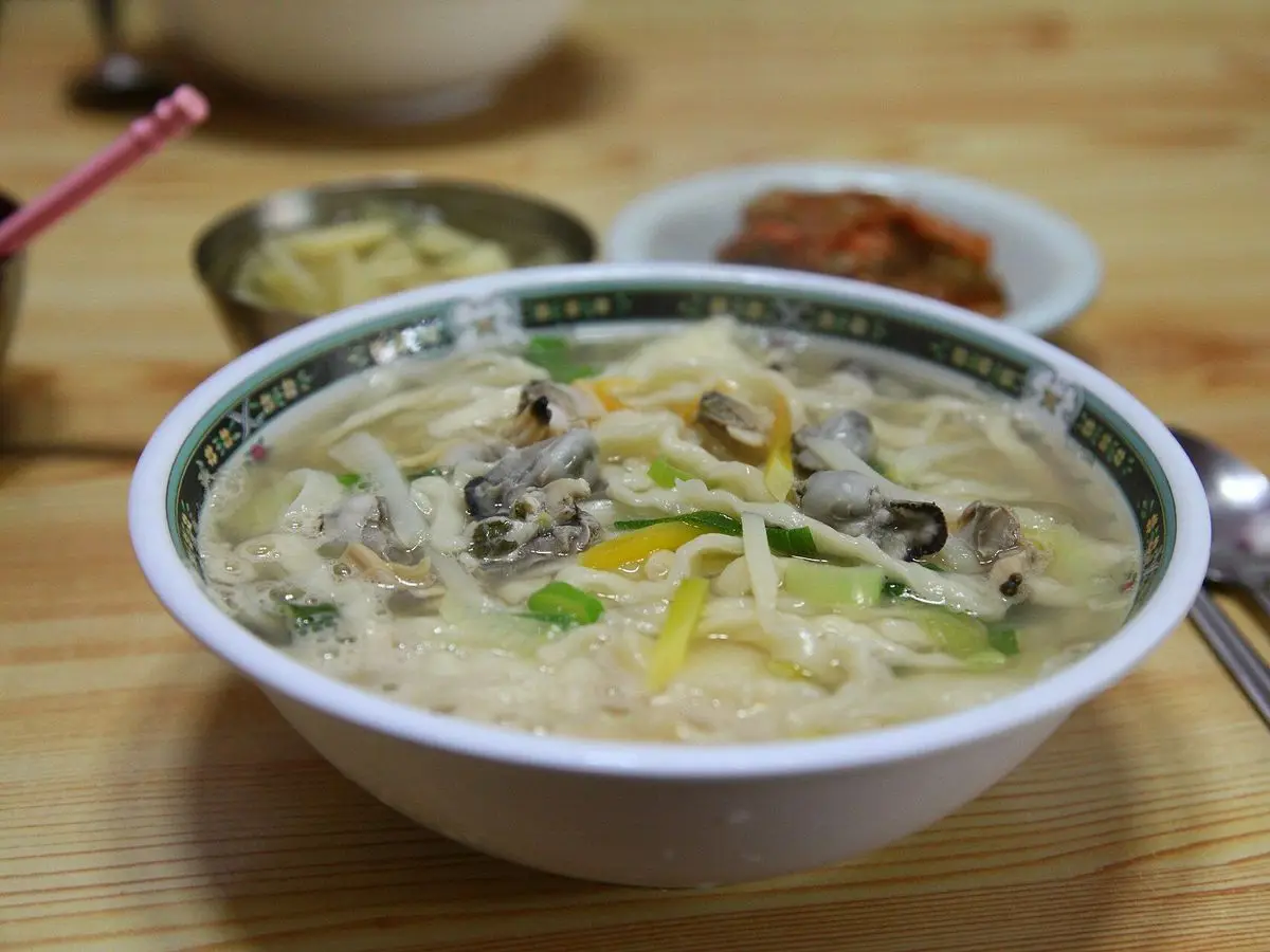 Cuenco de sopa coreana de fideos cortados a cuchillo con almejas y verduras sobre una mesa de madera