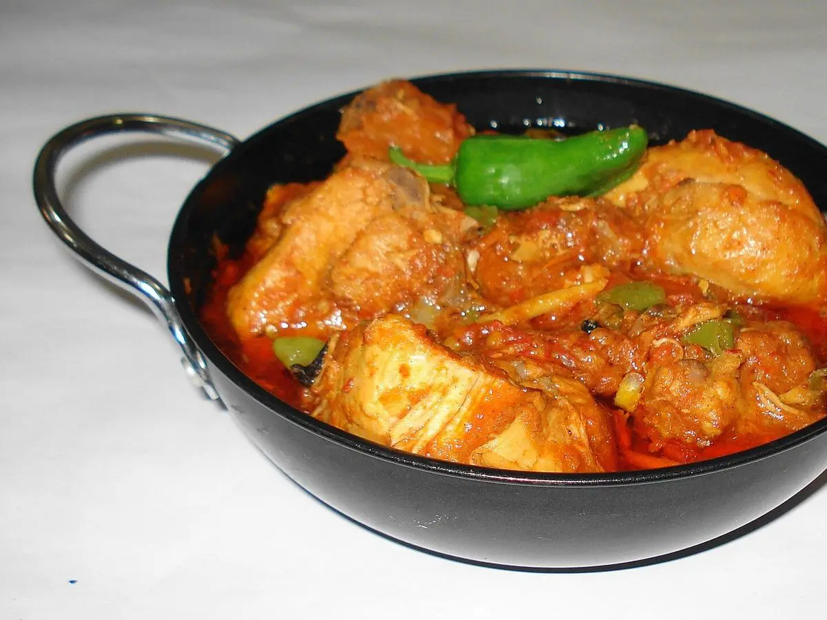 Karahi de pollo en salsa de tomate con guindillas verdes en una sartén negra de dos asas