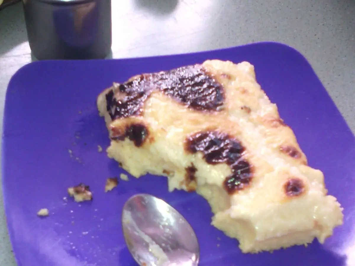 Porción dorada de karantika de garbanzo sobre plato morado con cuchara