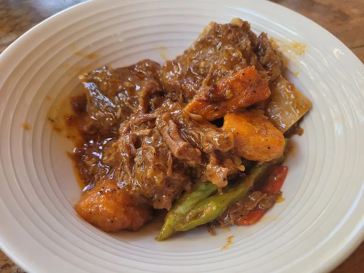 Plato blanco de carne de ternera guisada con calabaza y judías verdes en salsa espesa anaranjada