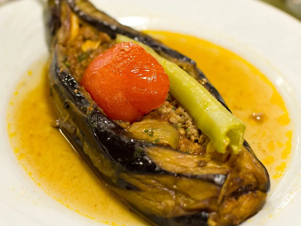Berenjena rellena de carne picada con tomate asado y pimiento verde sobre una salsa dorada