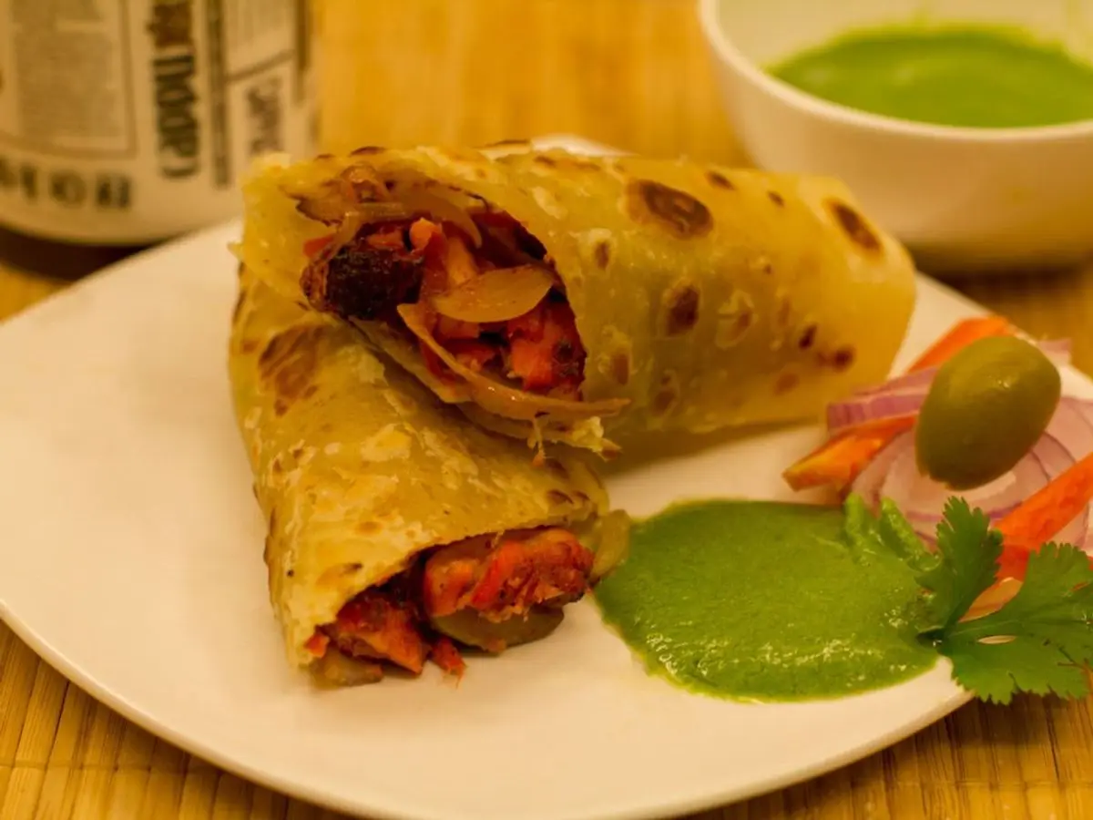 Rollo de pan plano relleno de pollo especiado con cebolla encurtida y salsa verde en un plato