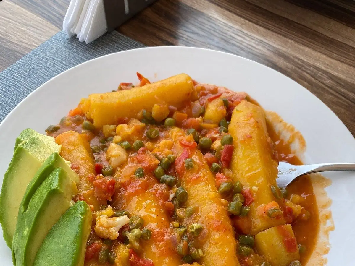 Plato con plátano macho guisado con tomate, guisantes y rodajas de aguacate