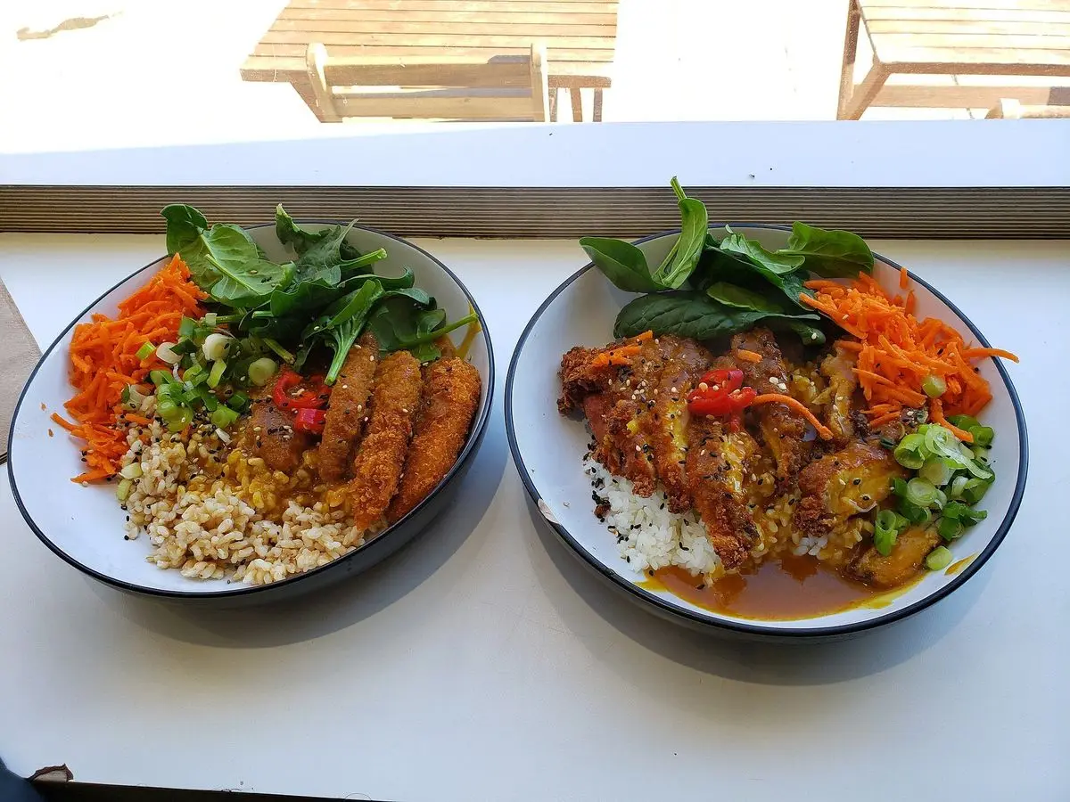 Dos cuencos de katsu curry con rebozado crujiente, arroz y verduras frescas sobre una mesa